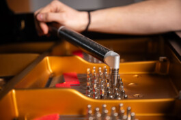 Detailfoto Stimmen am Flügel. Zu sehen ist ein aufgesetzter Stimmhammer , welcher mit einer Hand geführt wird. Im Wirbelfeld sind die einzelnen Stimmwirbel deutlich zu erkennen. 